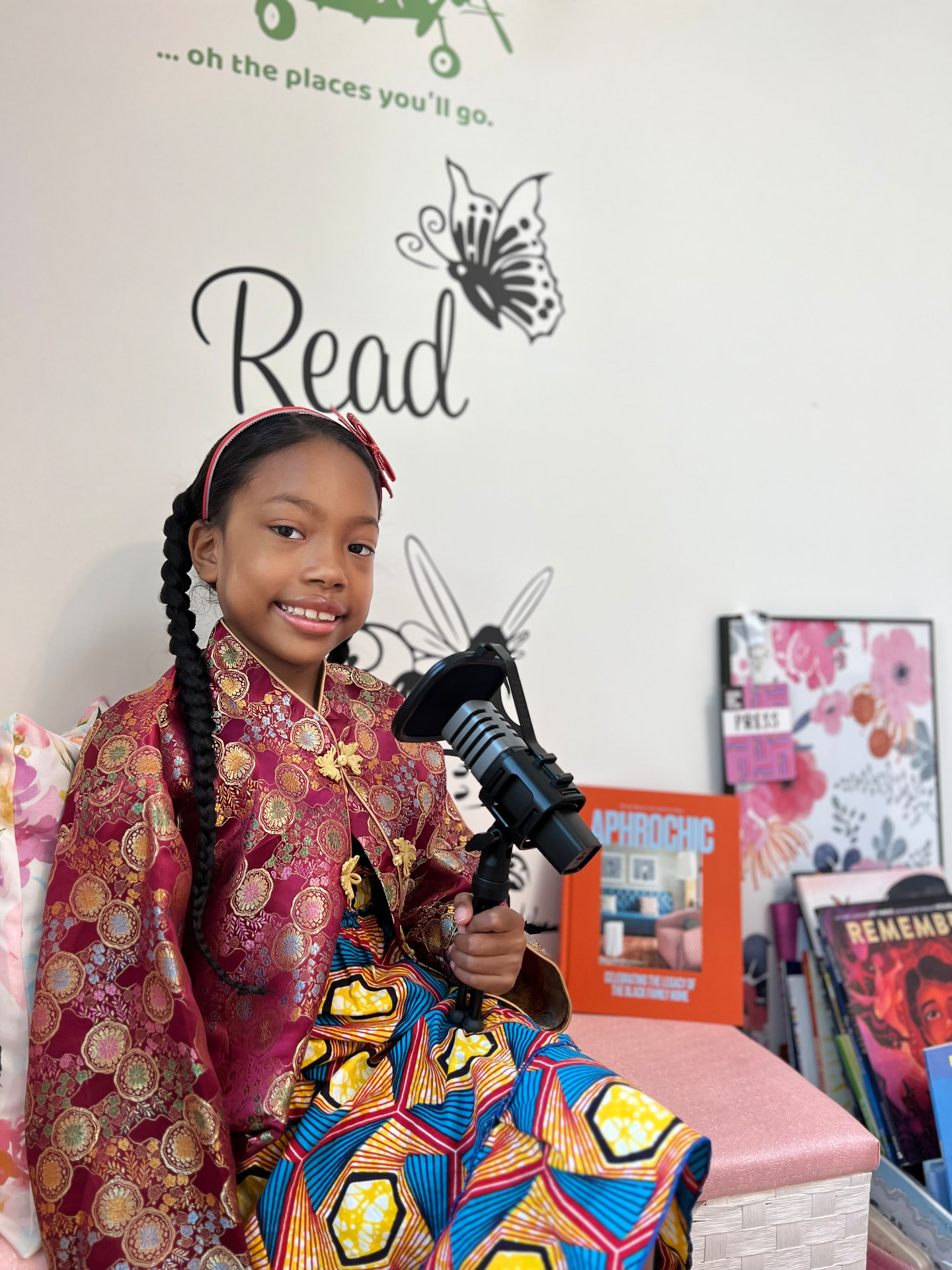 Ishara smiling in a colorful patterned outfit holding her podcast microphone