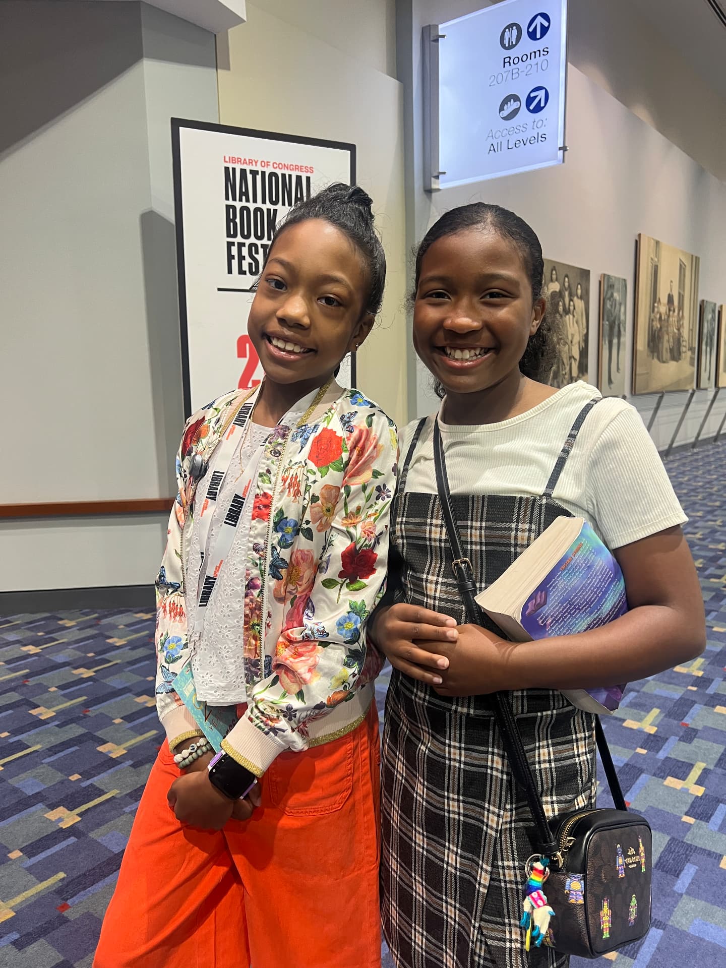 Ishara smiling with another young reader holding a book by the National Book Festival sign