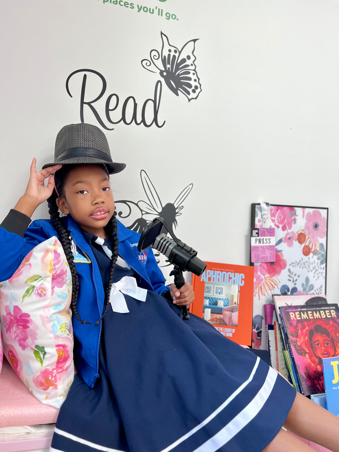 Ishara in a NASA jacket and hat holding her microphone in front of the Read wall