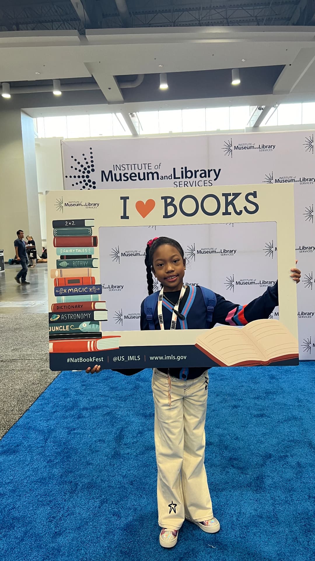 Ishara holding a large I love Books photo frame at the Institute of Museum and Library Services booth