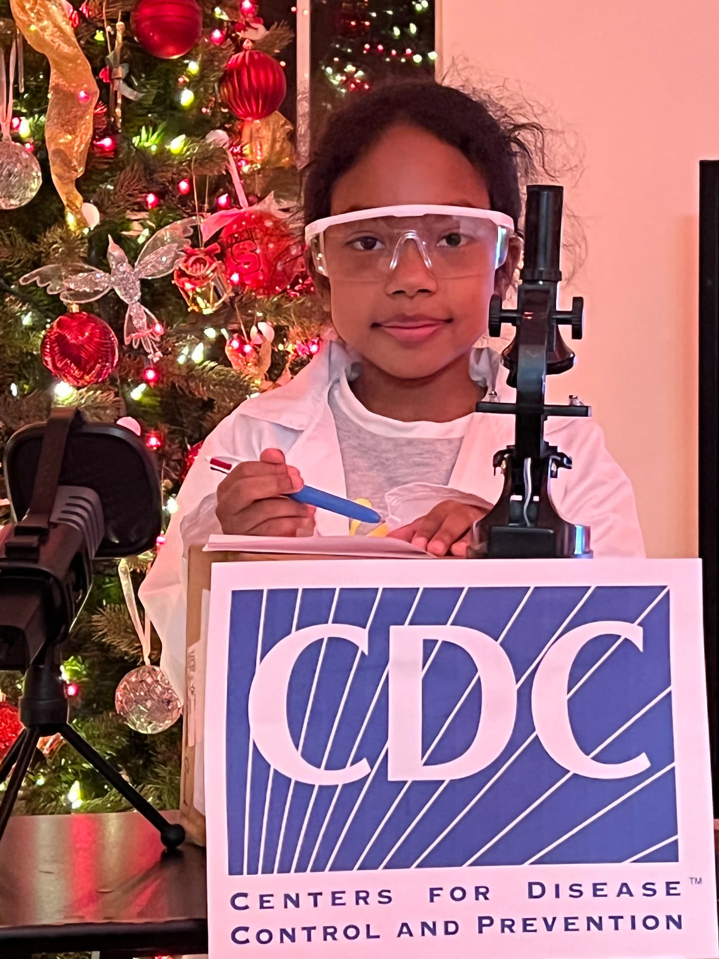 Ishara in a lab coat and safety goggles behind a CDC sign
