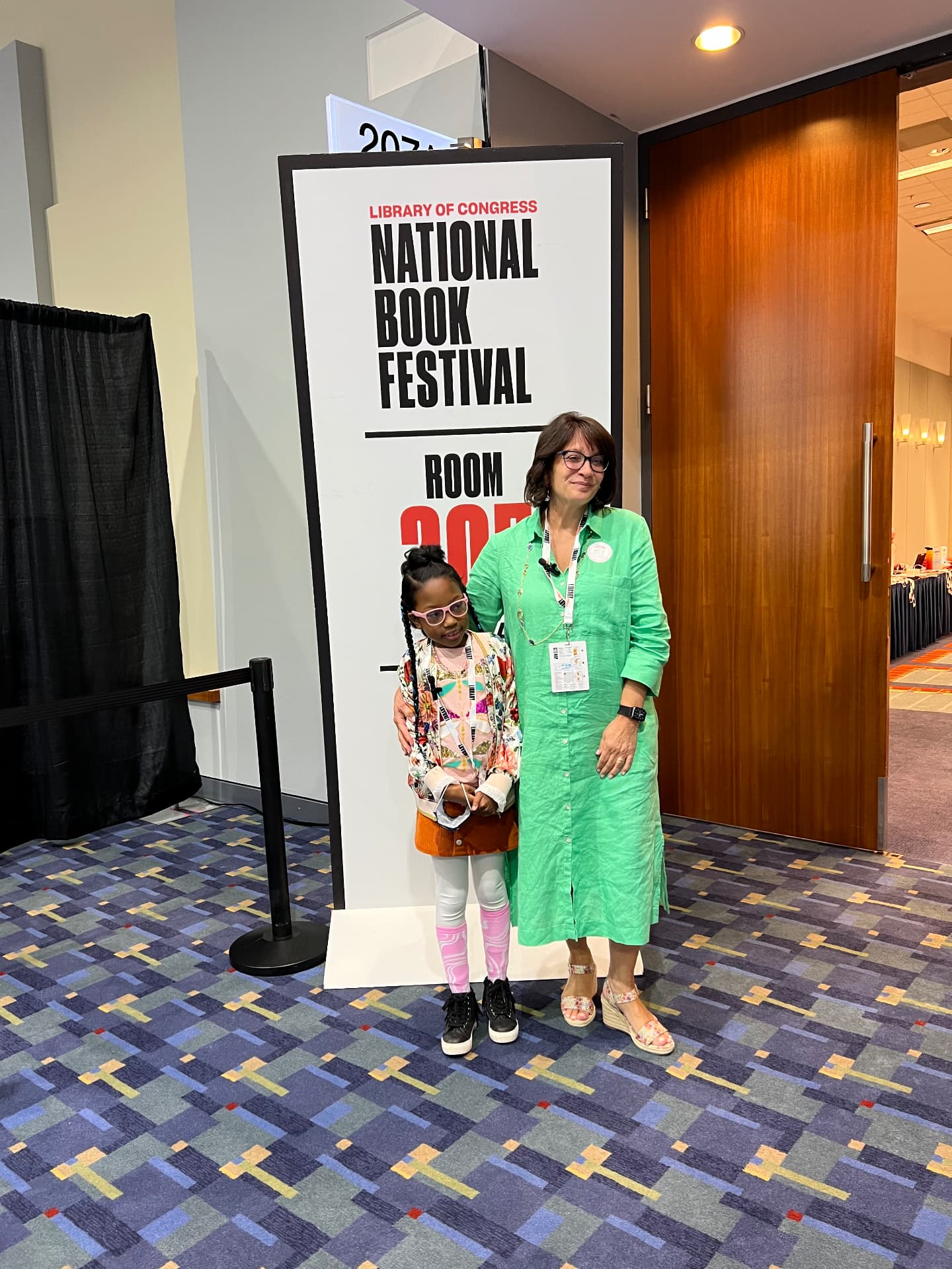 Ishara standing with an author beside a National Book Festival room sign