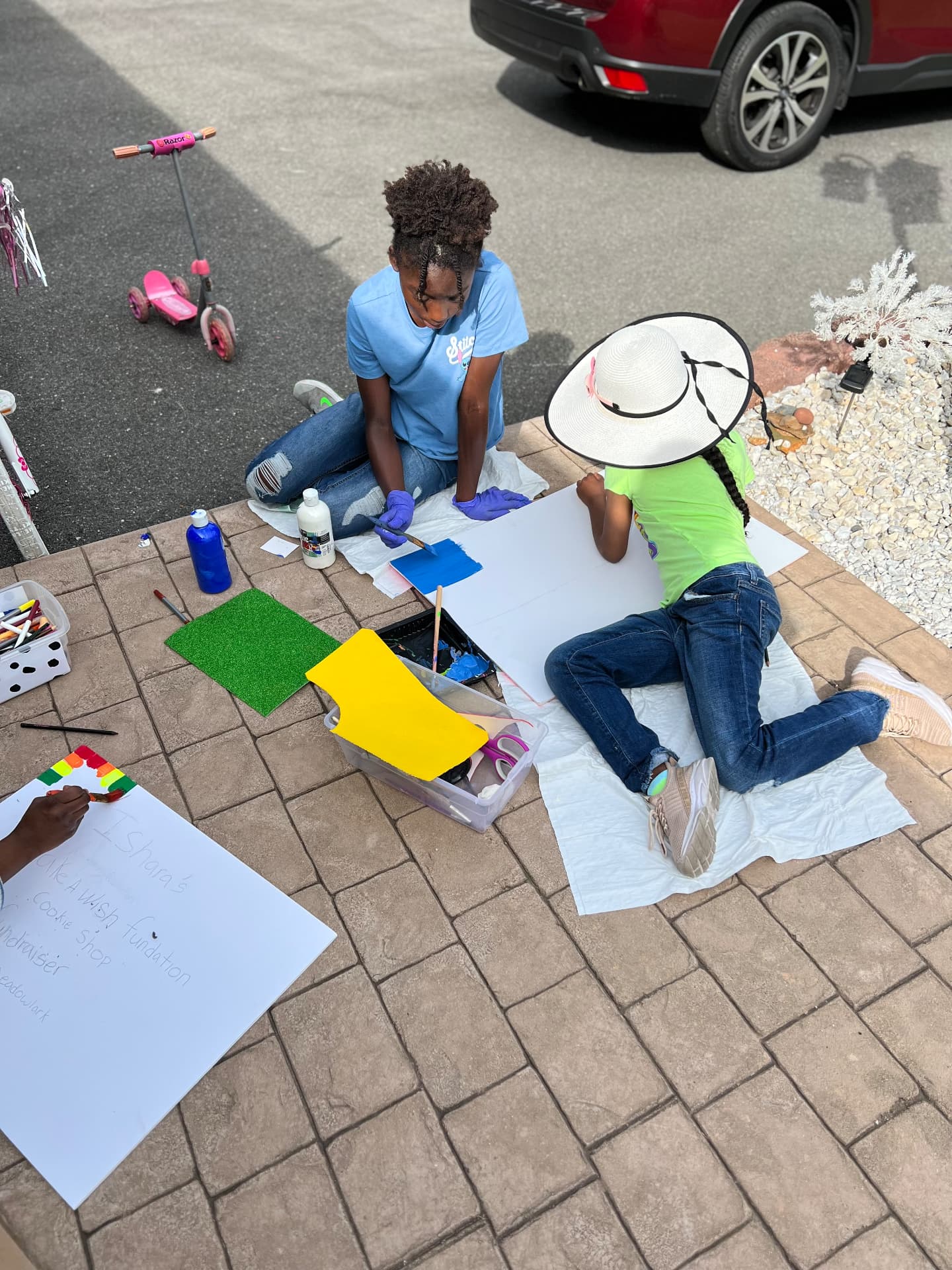 Ishara and a friend painting fundraiser signs on the driveway