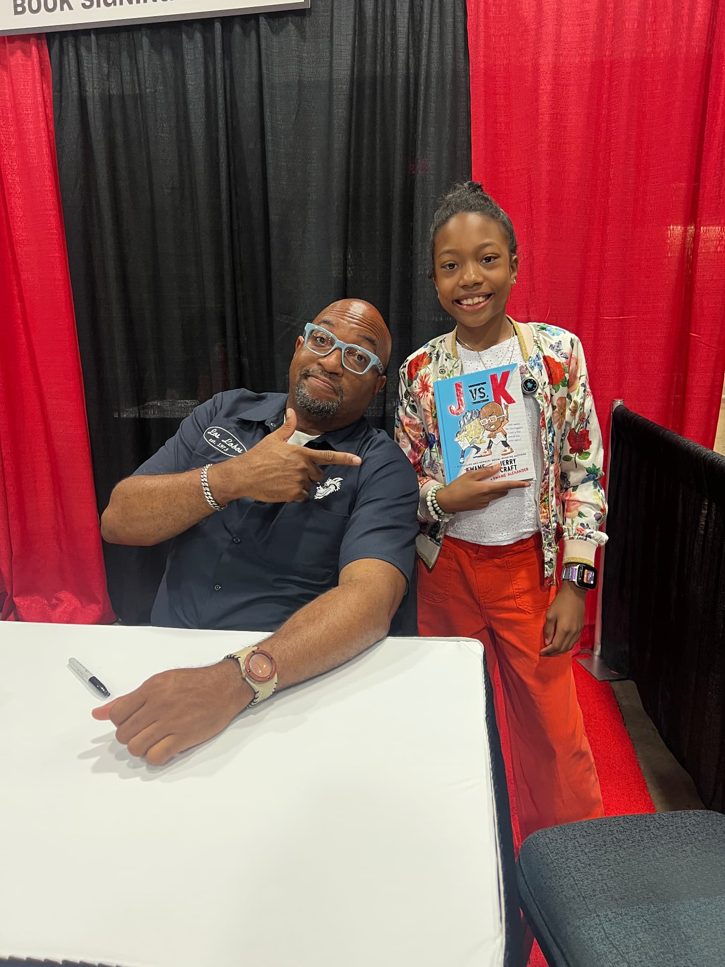 Ishara holding J vs. K next to author Jerry Craft at the book signing table