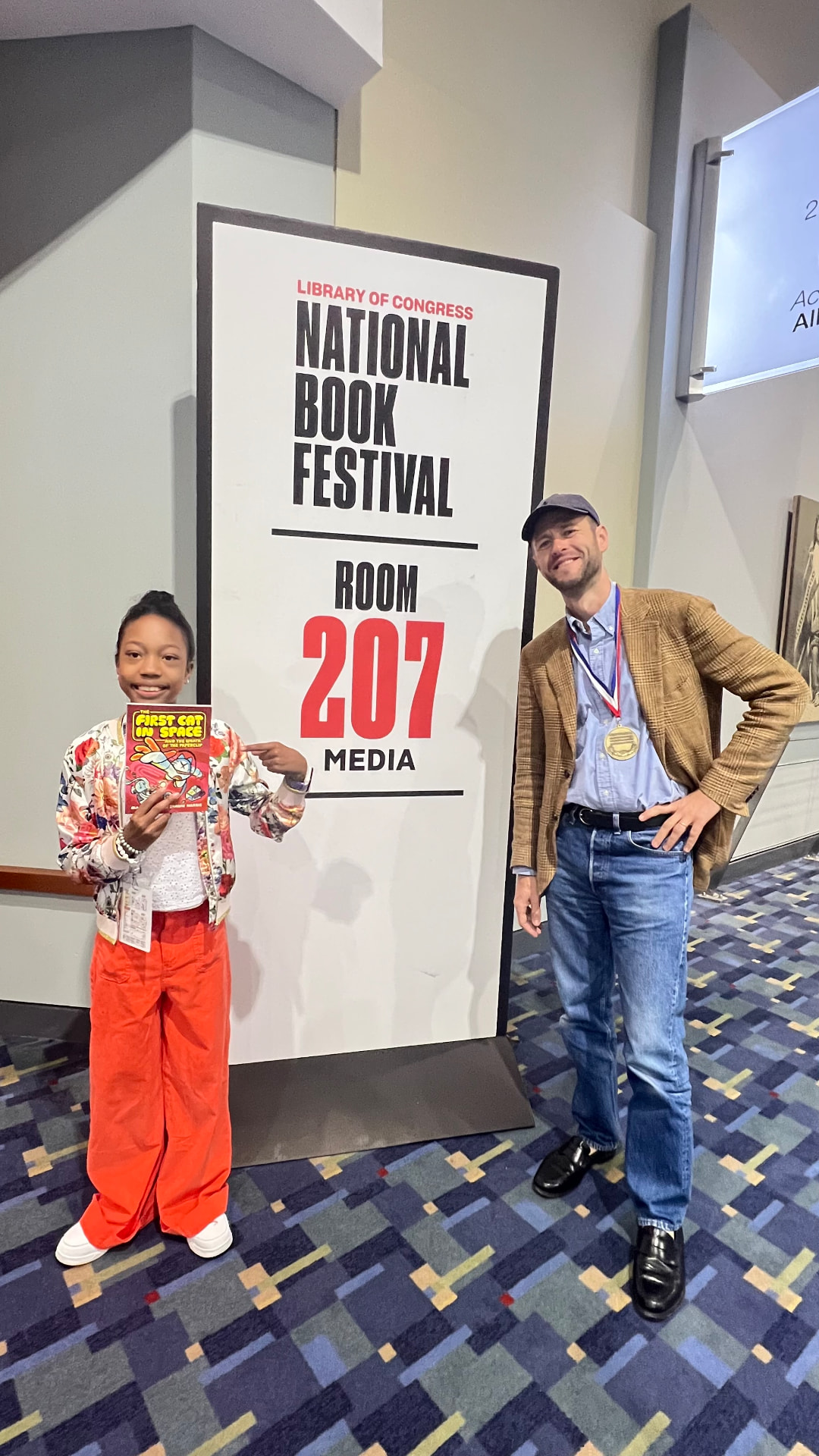 Ishara holding The First Cat in Space beside author Mac Barnett at the Room 207 Media sign